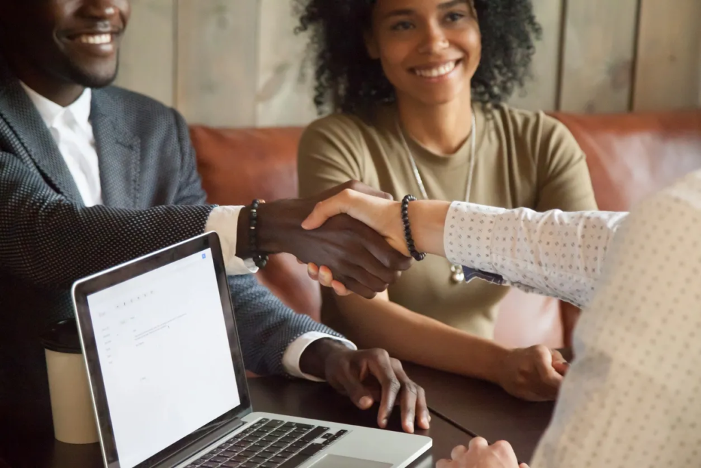 A woman shaking hands with another person over a laptop.