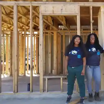 Two women standing in front of a wall.