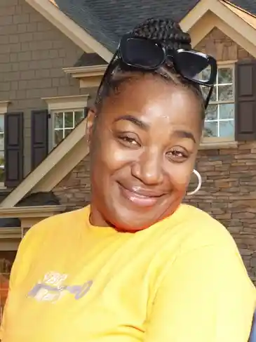 A woman in yellow shirt and sunglasses smiling.