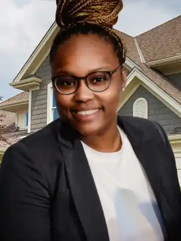 A woman in glasses and a jacket standing outside of a house.