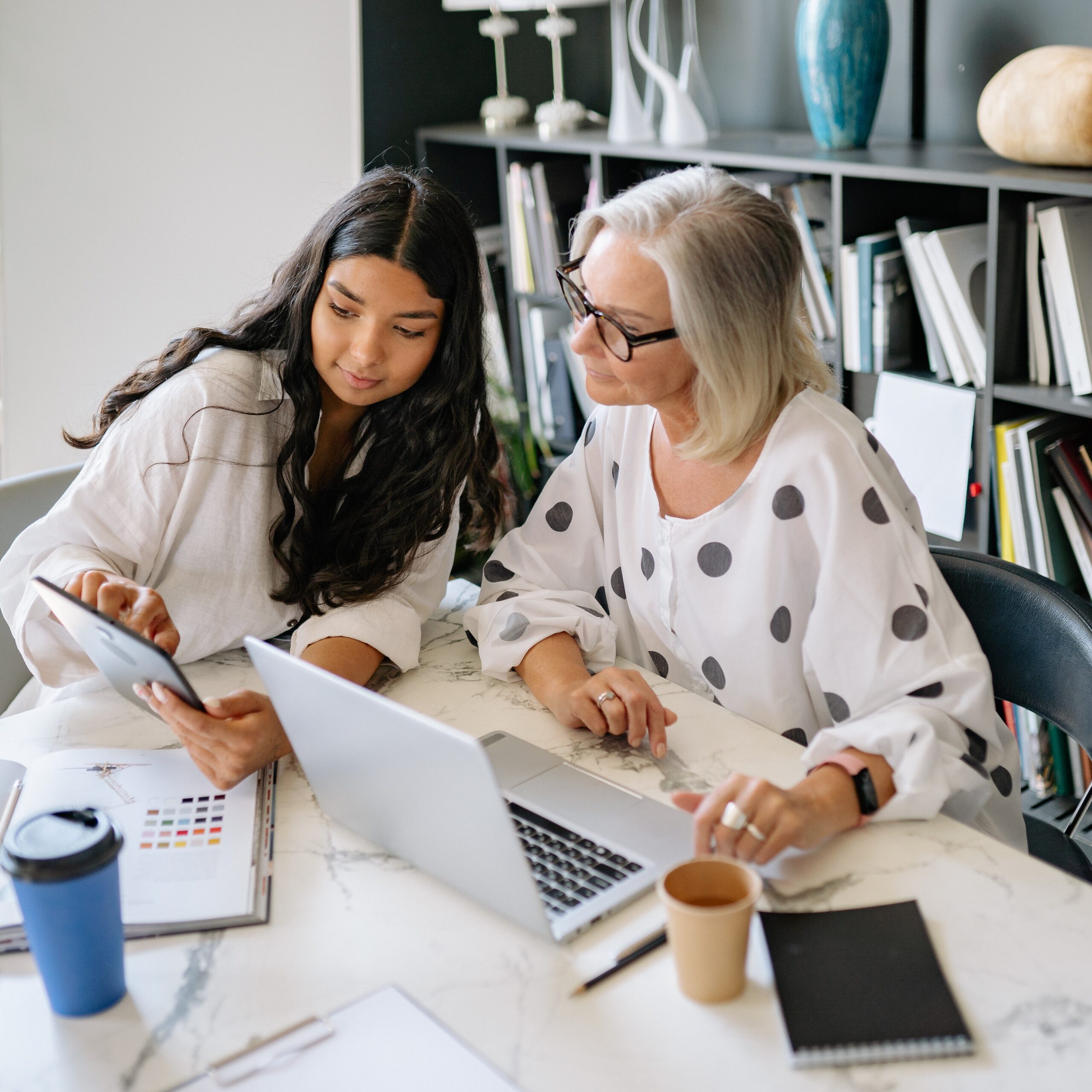 Two women sitting at a table with laptops.